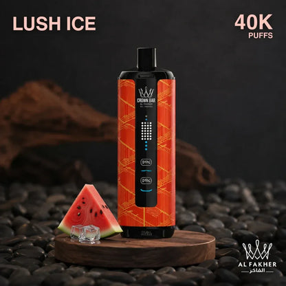 A Crown Daiv disposable vape device in 'Lush Ice' flavor, featuring a black body with a vibrant orange and red patterned side. It is displayed on a wooden stand next to a slice of watermelon on a bed of dark pebbles, with text overlays 'LUSH ICE', '40K PUFFS', and the 'AL FAKHER' brand logo.